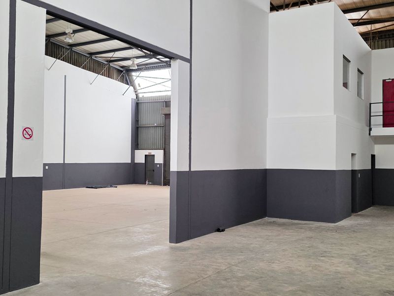 Spacious industrial warehouse unit featuring high ceilings with exposed steel trusses, concrete flooring, and a mezzanine level with integrated staircase access.