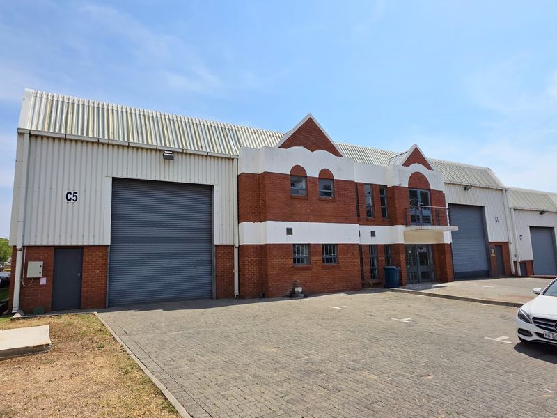 Front elevation of an industrial warehouse unit featuring brick and metal cladding, roller shutter doors, and a paved parking area.