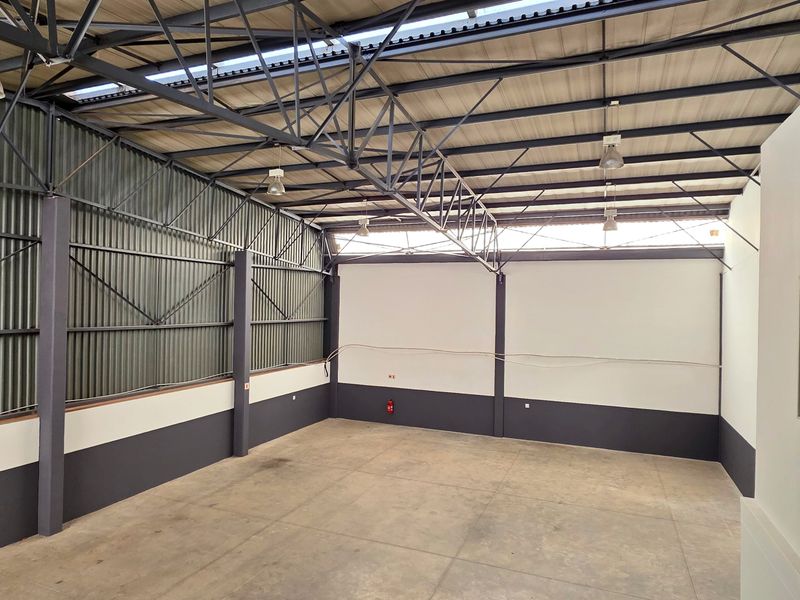 Spacious industrial utility area featuring high ceilings with exposed steel trusses, corrugated metal wall cladding, and durable concrete flooring.