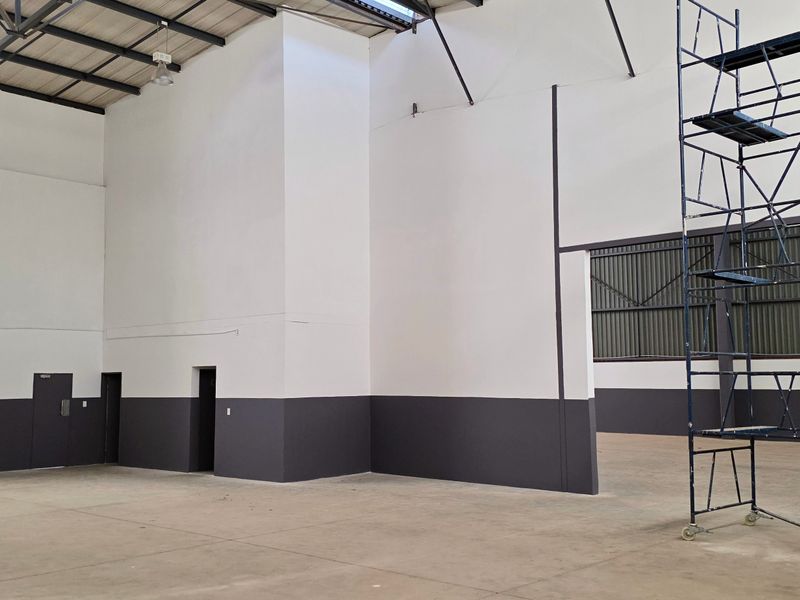 Spacious industrial warehouse unit featuring high ceilings with exposed steel trusses, concrete flooring, and clean painted walls, suitable for various commercial or storage uses.