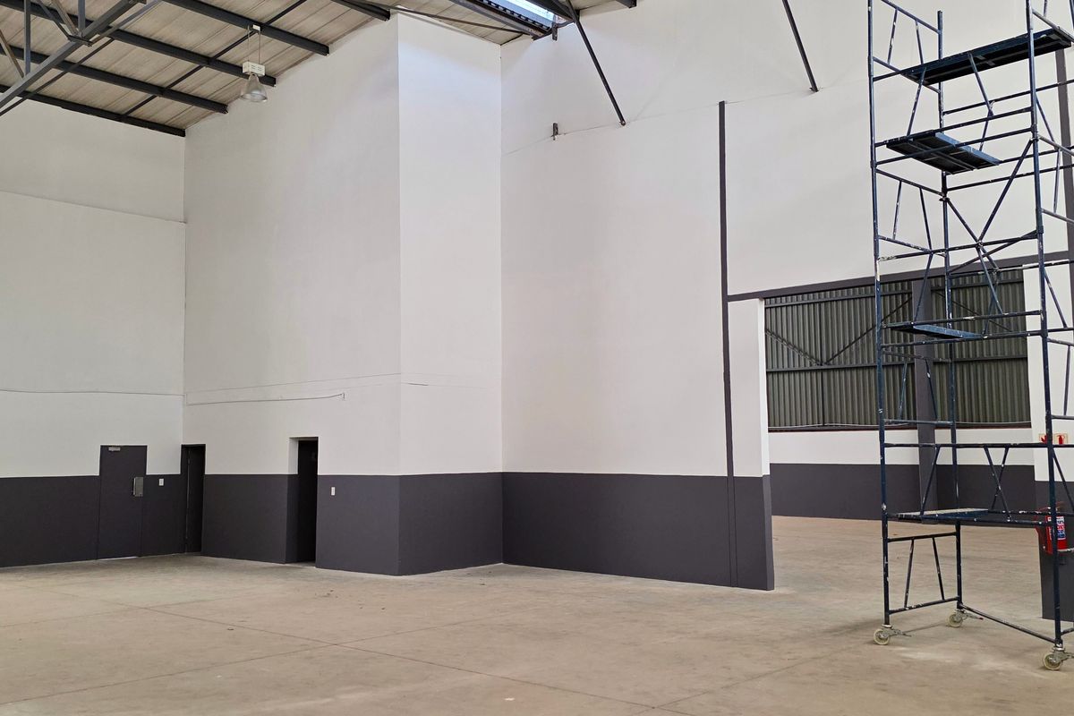 Spacious industrial warehouse unit featuring high ceilings with exposed steel trusses, concrete flooring, and clean painted walls, suitable for various commercial or storage uses.