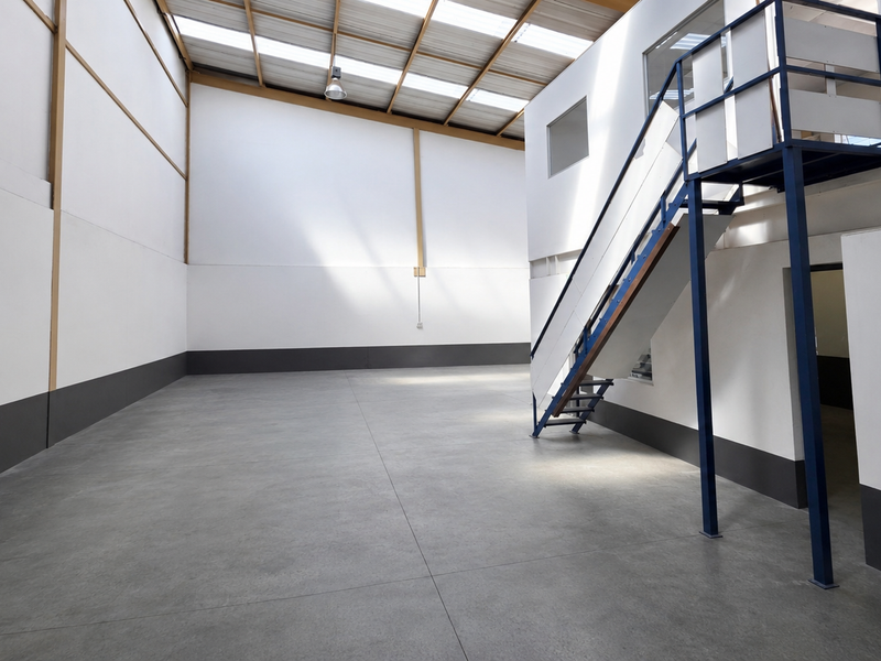 Spacious industrial warehouse unit featuring polished concrete floors, high ceilings with skylights, and a built-in mezzanine level with a metal staircase.