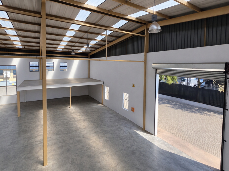 Spacious industrial warehouse unit featuring a mezzanine level, concrete flooring, high-clearance steel frame, and a large roller shutter door for easy access.