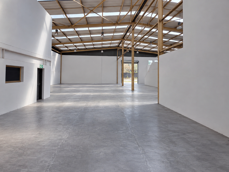 Spacious industrial warehouse unit featuring high ceilings with exposed steel trusses, translucent roof panels for natural light, and polished concrete flooring.