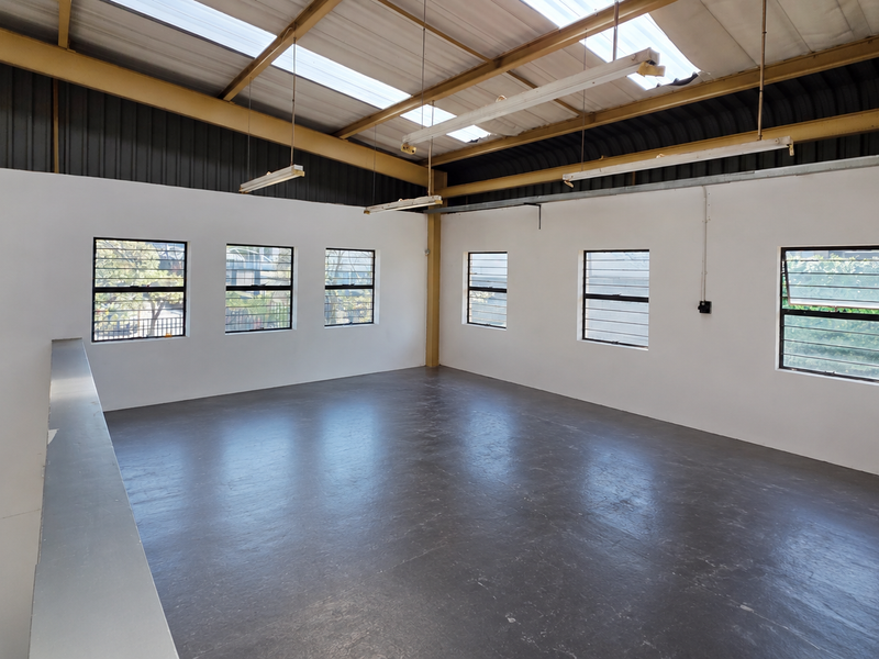 Spacious industrial mezzanine area featuring exposed steel roof trusses, natural light through translucent panels, and durable painted concrete flooring.