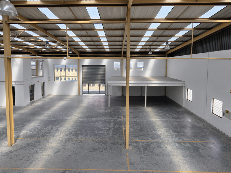 Spacious industrial warehouse featuring a high-clearance steel portal frame, mezzanine level, roller shutter door, and abundant natural light through integrated roof skylights.