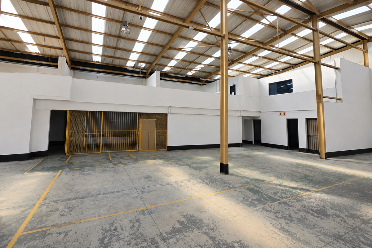 Spacious industrial utility area featuring a high steel portal frame roof, translucent panels for natural light, concrete flooring, and a secure caged storage section.