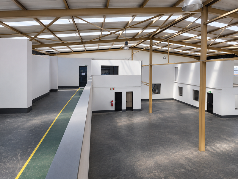 Spacious industrial open-plan warehouse featuring high ceilings with exposed steel trusses, abundant natural light from skylights, and a functional mezzanine level.