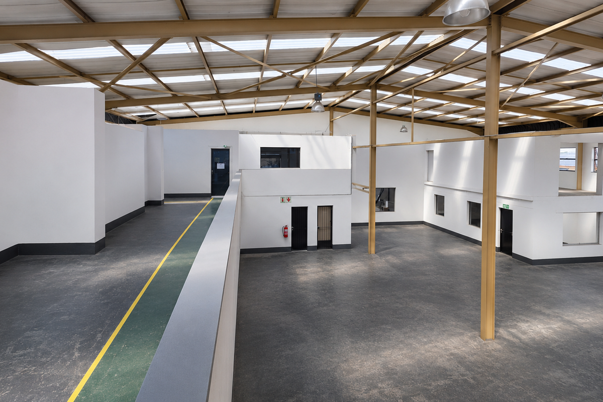 Spacious industrial open-plan warehouse featuring high ceilings with exposed steel trusses, abundant natural light from skylights, and a functional mezzanine level.