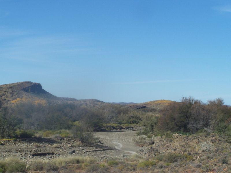 A scenic landscape view of the farm property featuring natural terrain, rocky outcrops, and indigenous vegetation under a clear blue sky.