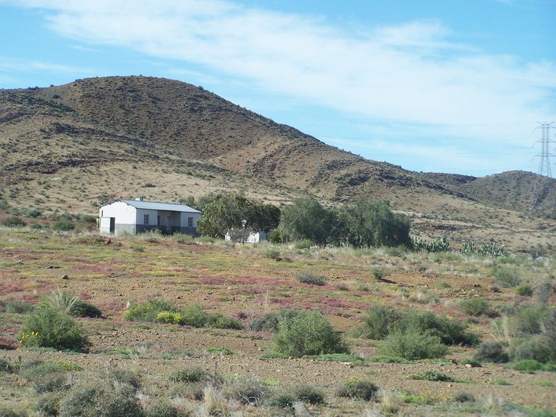A distant view of a rural farm dwelling set against a mountainous landscape with natural vegetation.