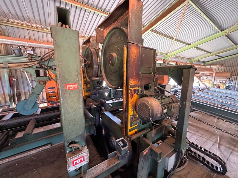 Industrial workshop space featuring heavy-duty band saw machinery housed within a corrugated metal structure.