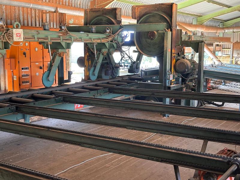 Industrial sawmill facility featuring heavy-duty timber processing machinery, conveyor systems, and integrated electrical control infrastructure within a large metal-framed shed.