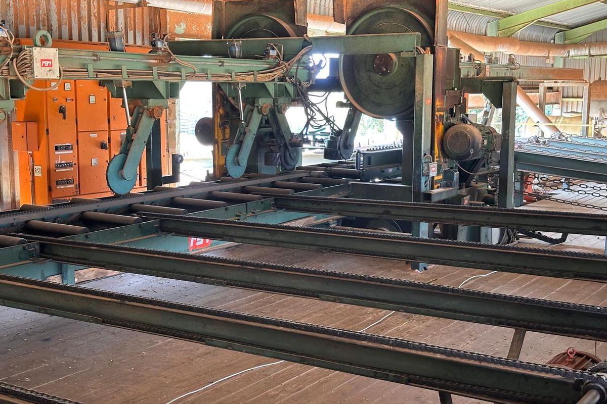 Industrial sawmill facility featuring heavy-duty timber processing machinery, conveyor systems, and integrated electrical control infrastructure within a large metal-framed shed.