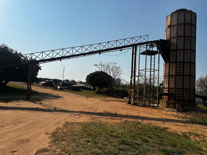 An industrial farm silo with an attached metal conveyor structure and support frame located on a dirt track.
