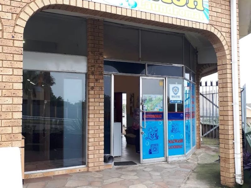 Front entrance of a commercial laundromat featuring a brick facade, arched entryway, and glass storefront with signage.