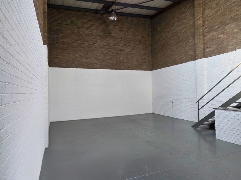 Spacious industrial utility area featuring high ceilings, exposed brickwork, painted masonry walls, durable epoxy flooring, and a metal staircase.