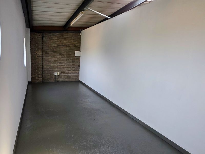 A clean, empty industrial-style office space featuring exposed brickwork, polished epoxy flooring, exposed ceiling beams, and distinctive porthole windows.