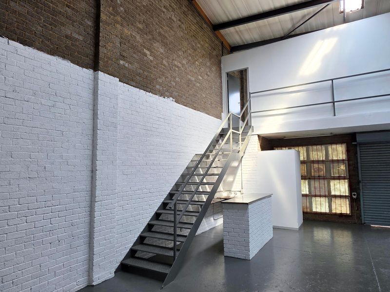 Spacious industrial utility area featuring exposed brick walls, a metal staircase leading to a mezzanine level, and a secure roller shutter door.
