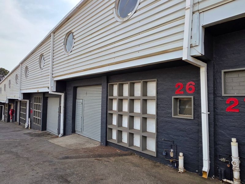 Exterior view of an industrial complex featuring multiple units with roller shutter doors, metal cladding, and painted brick facades.