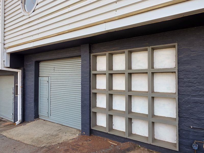 Industrial unit exterior featuring a roller shutter door, metal cladding, and a distinctive decorative grid screen facade.