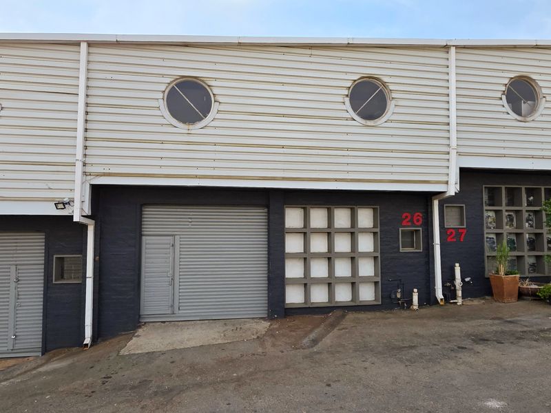 Front elevation of an industrial property featuring roller shutter doors, metal cladding, and circular windows, providing functional access for commercial or warehouse use.