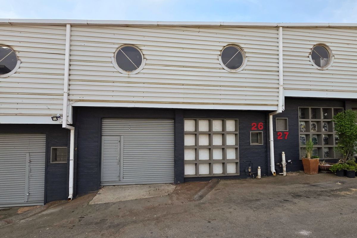 Front elevation of an industrial property featuring roller shutter doors, metal cladding, and circular windows, providing functional access for commercial or warehouse use.