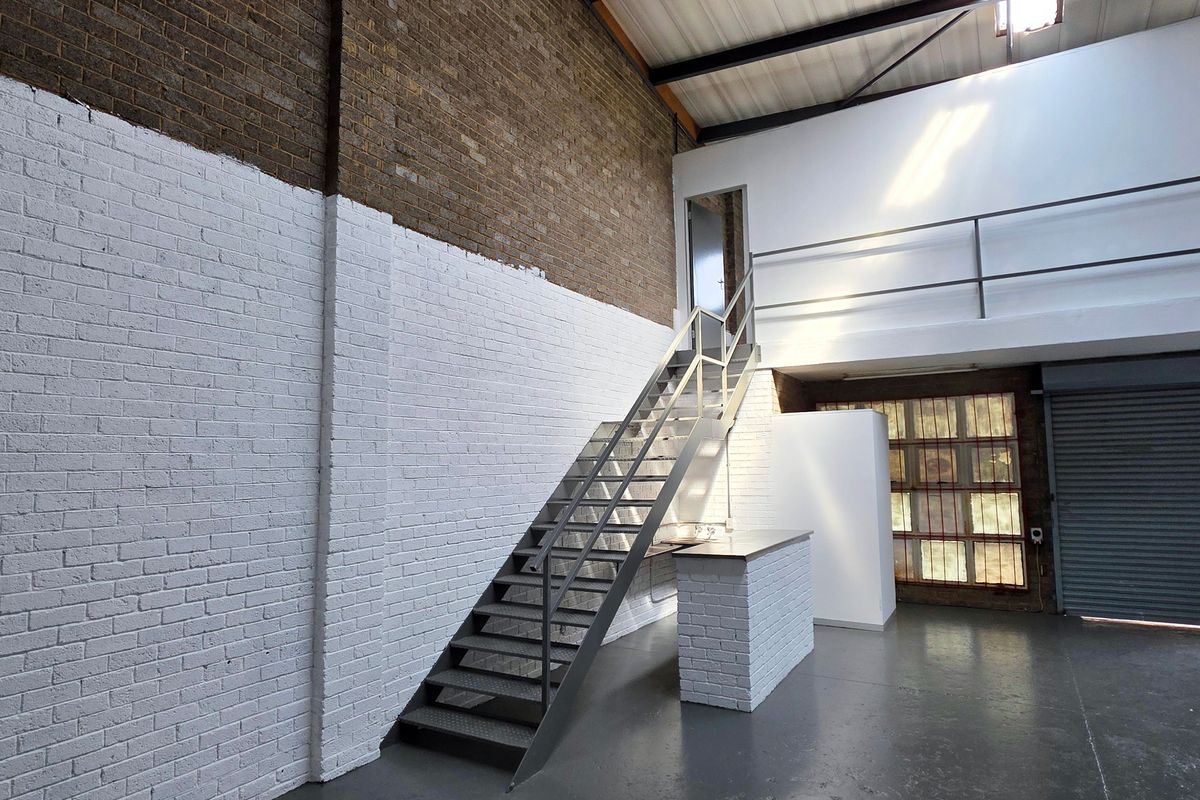 Spacious industrial utility area featuring exposed brick walls, a metal staircase leading to a mezzanine level, and a large roller shutter door.