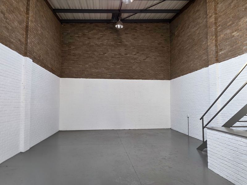 Spacious industrial utility area featuring high ceilings with exposed steel trusses, painted brick walls, durable concrete flooring, and a metal staircase.