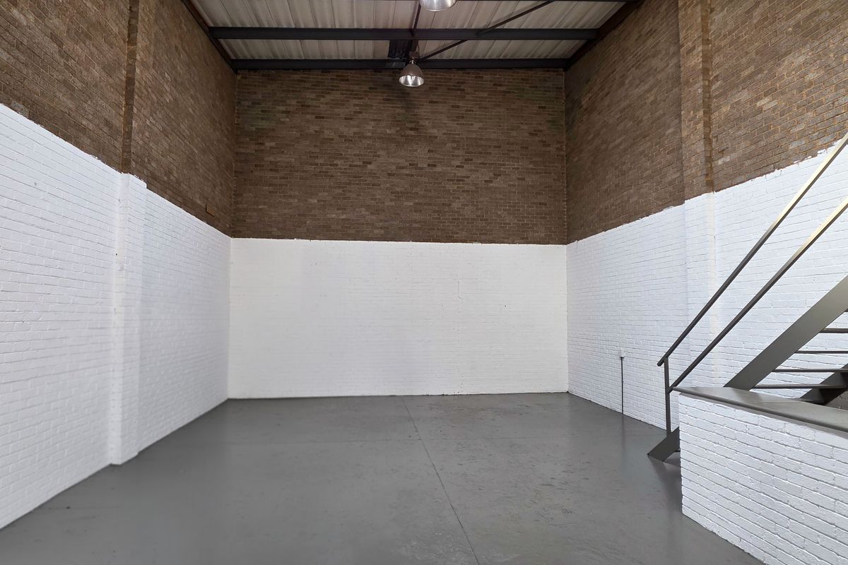 Spacious industrial utility area featuring high ceilings with exposed steel trusses, painted brick walls, durable concrete flooring, and a metal staircase.