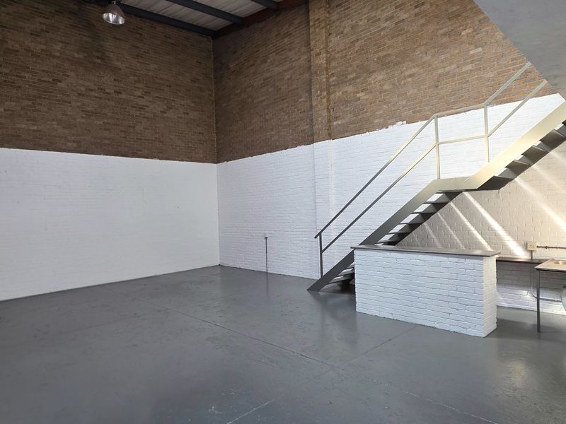 Spacious industrial utility area featuring exposed brickwork, durable epoxy flooring, a metal staircase, and a built-in sink station.