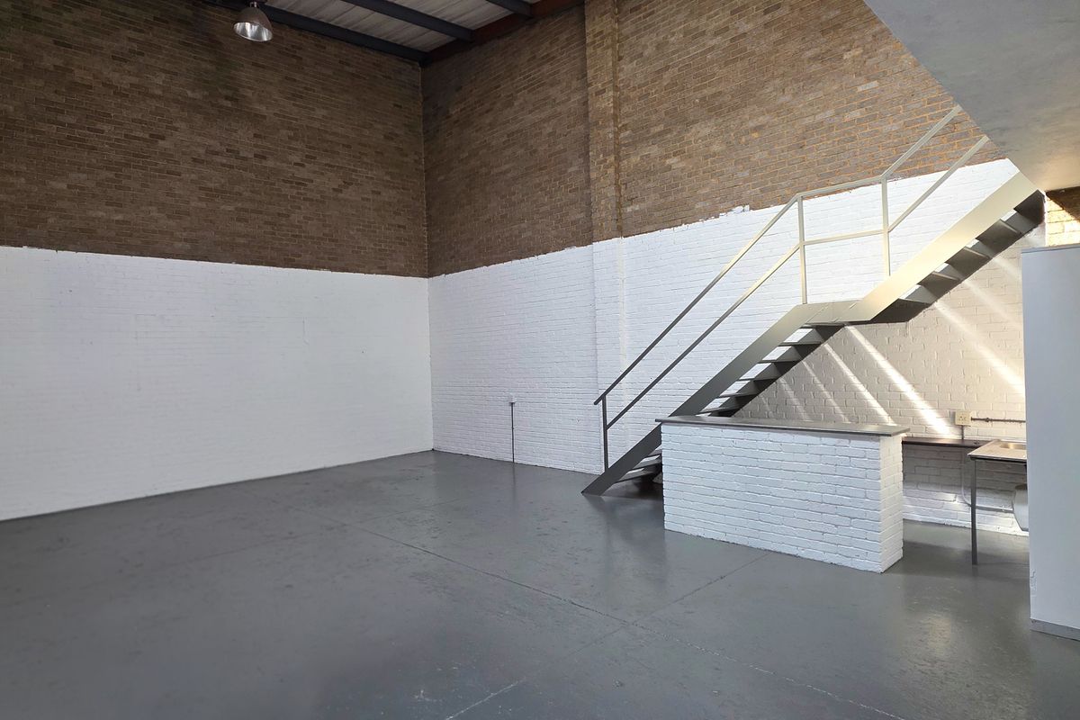 Spacious industrial utility area featuring exposed brickwork, durable epoxy flooring, a metal staircase, and a built-in sink station.