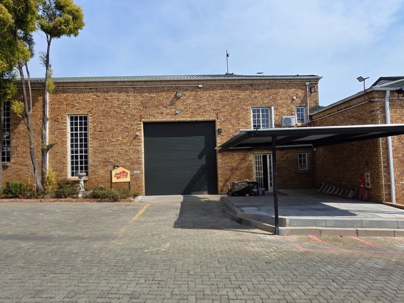 Industrial property featuring a face brick facade, large roller shutter door, paved driveway, and a covered parking area.