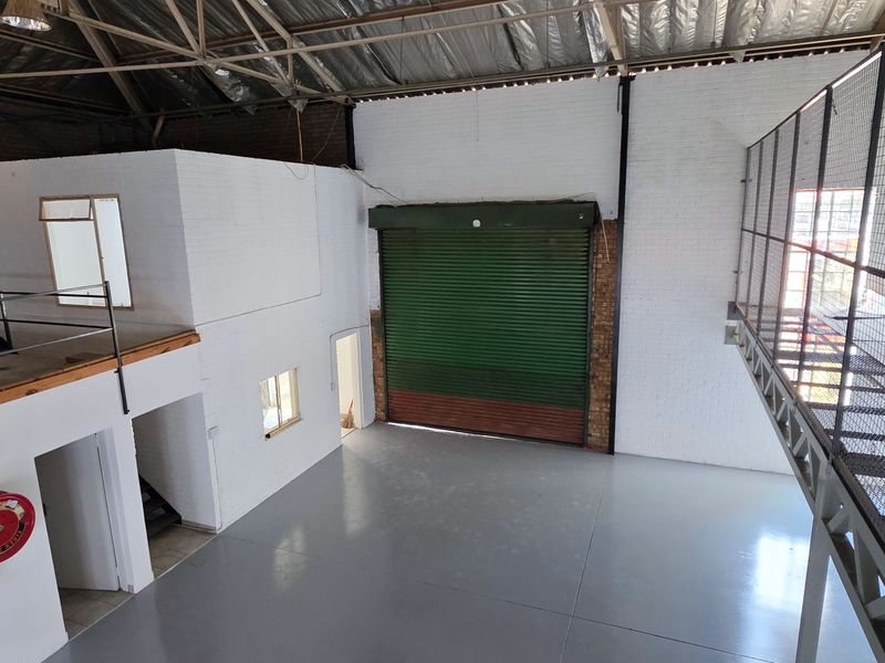 Spacious industrial warehouse unit featuring a high-clearance ceiling, roller shutter door, mezzanine level with safety railing, and durable epoxy flooring.