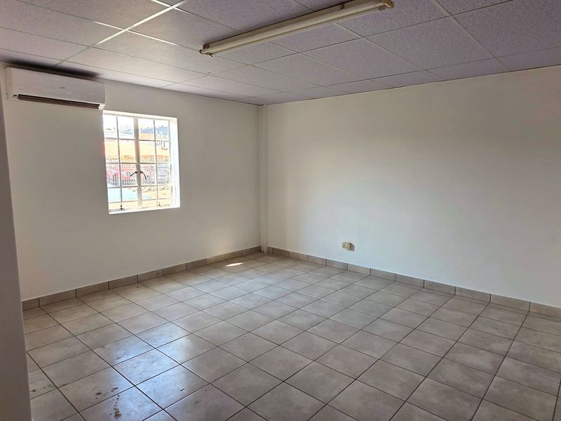 A clean, empty office space featuring ceramic floor tiles, a suspended ceiling, and a wall-mounted air conditioning unit.