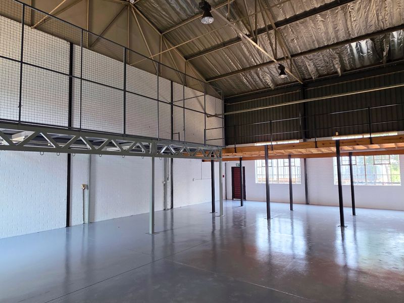 Spacious industrial warehouse unit featuring a mezzanine level, high exposed ceilings, durable epoxy flooring, and ample natural light through large windows.
