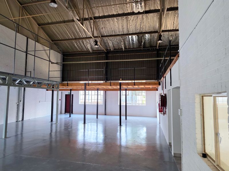 Spacious industrial warehouse unit featuring high ceilings with exposed steel trusses, a mezzanine level, and durable epoxy-coated concrete flooring.