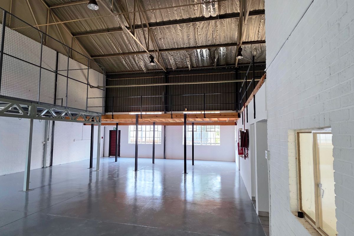 Spacious industrial warehouse unit featuring high ceilings with exposed steel trusses, a mezzanine level, and durable epoxy-coated concrete flooring.