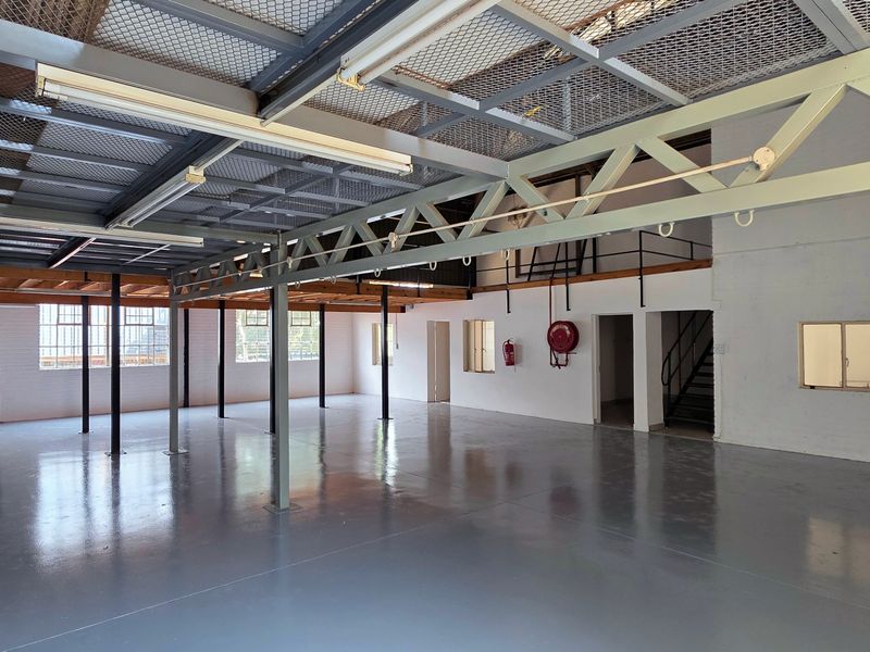 Spacious industrial open-plan warehouse area featuring a mezzanine level, durable epoxy flooring, steel structural trusses, and secure access points.