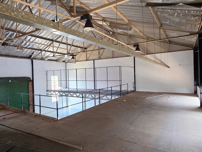 Spacious industrial mezzanine area featuring exposed steel roof trusses, high ceilings, and metal safety railings, suitable for storage or workshop conversion.