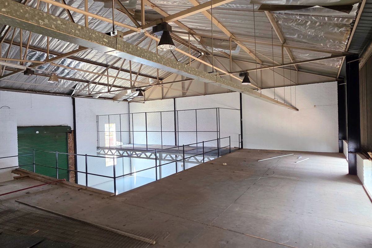 Spacious industrial mezzanine area featuring exposed steel roof trusses, high ceilings, and metal safety railings, suitable for storage or workshop conversion.