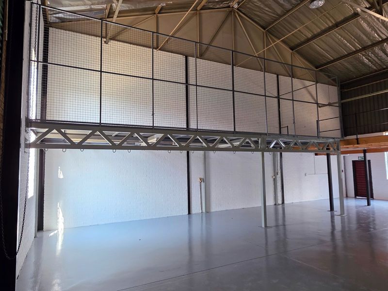 Spacious industrial warehouse unit featuring a mezzanine level, high ceilings with exposed steel trusses, and durable epoxy-coated concrete flooring.