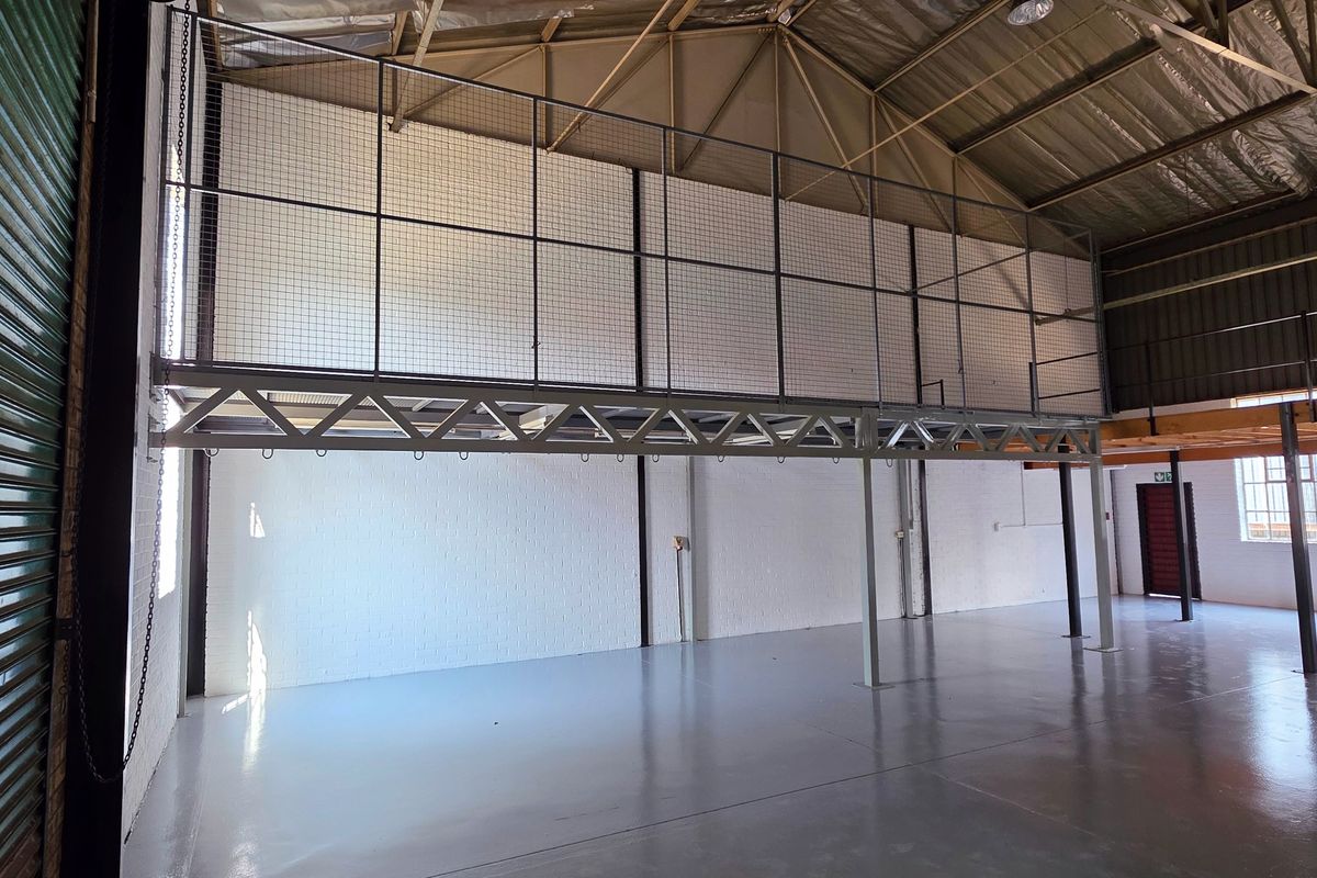 Spacious industrial warehouse unit featuring a mezzanine level, high ceilings with exposed steel trusses, and durable epoxy-coated concrete flooring.