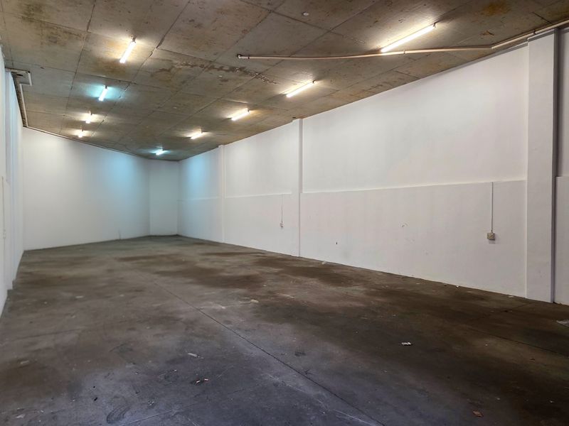 A spacious, empty industrial utility area featuring an exposed concrete ceiling, fluorescent lighting, and durable concrete flooring, suitable for storage or workshop use.