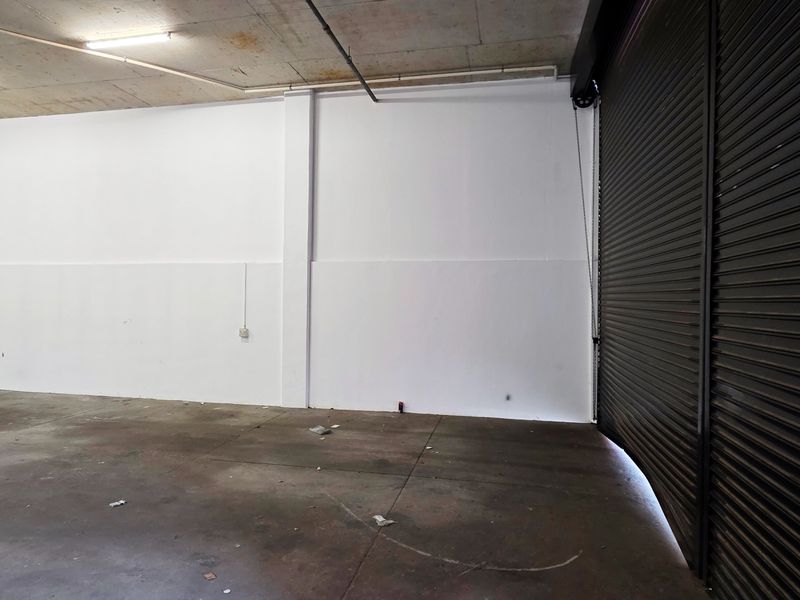 Spacious industrial garage featuring a large roller shutter door, exposed concrete ceiling, and durable concrete flooring, suitable for storage or workshop use.