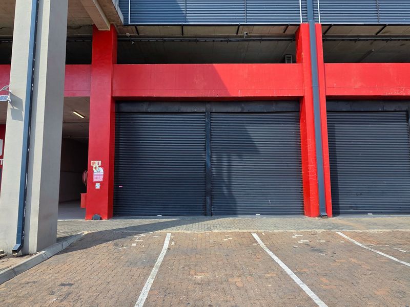 Front elevation of an industrial property featuring multiple roller shutter doors, concrete structural columns, and a paved parking area.