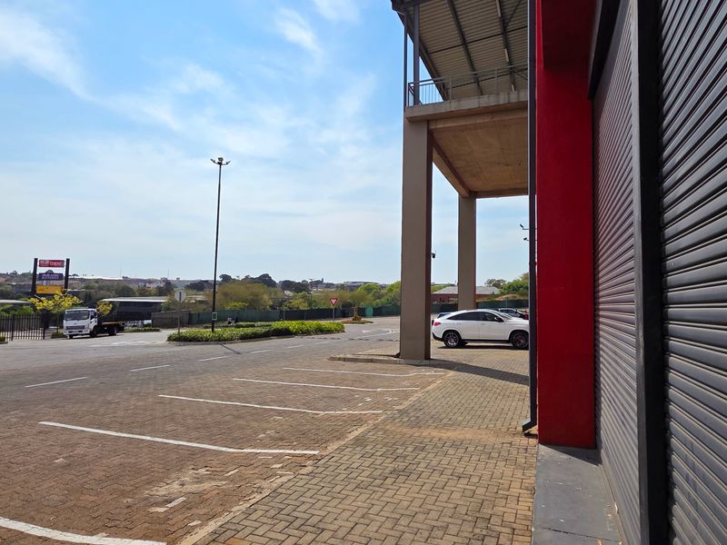 Exterior view of an industrial property featuring a roller shutter door, paved parking area, and concrete structural columns under a metal roof canopy.