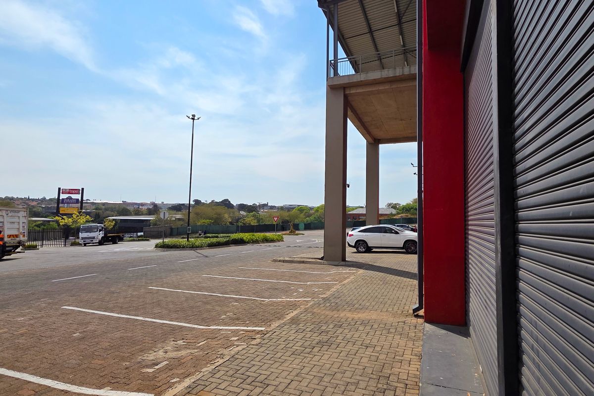Exterior view of an industrial property featuring a roller shutter door, paved parking area, and concrete structural columns under a metal roof canopy.