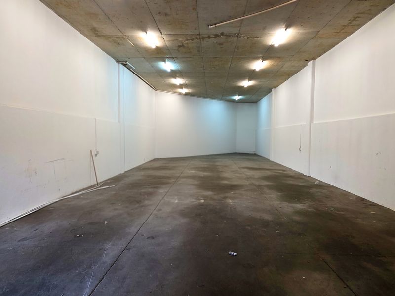 An empty industrial utility space featuring an exposed concrete ceiling, concrete flooring, and surface-mounted lighting, suitable for storage or workshop use.