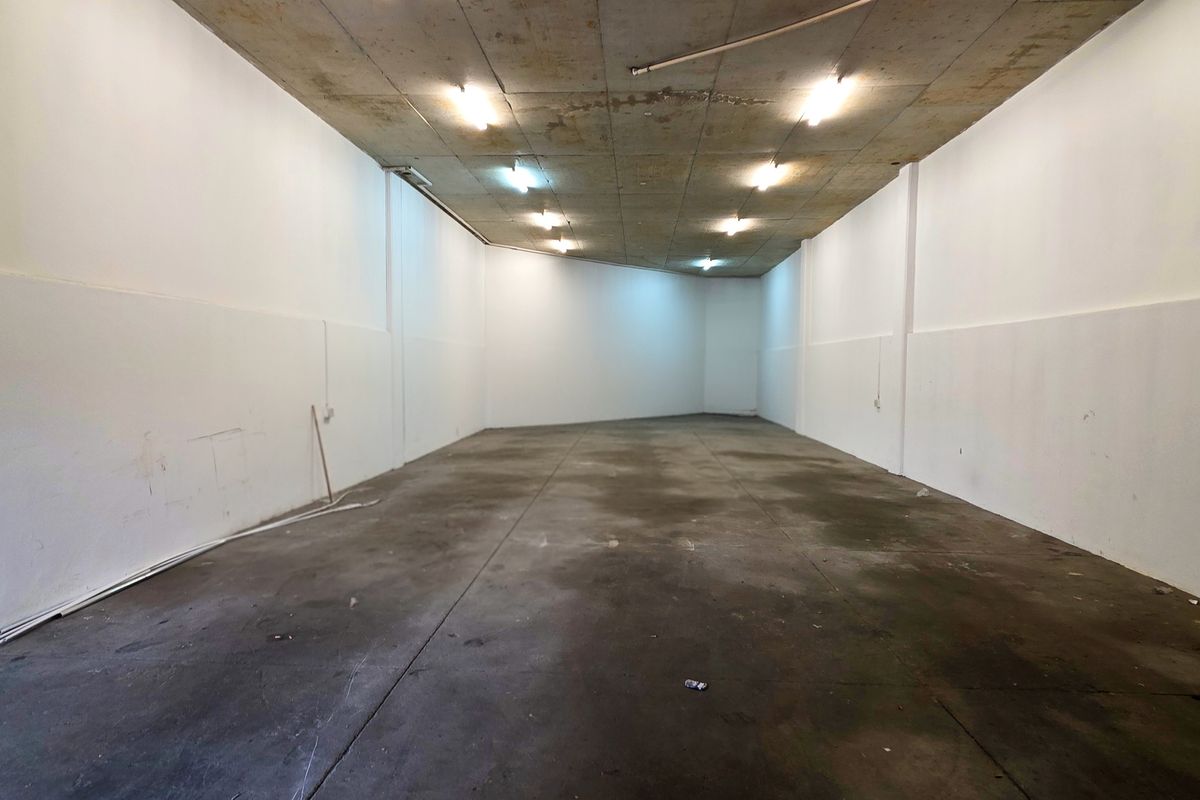 An empty industrial utility space featuring an exposed concrete ceiling, concrete flooring, and surface-mounted lighting, suitable for storage or workshop use.